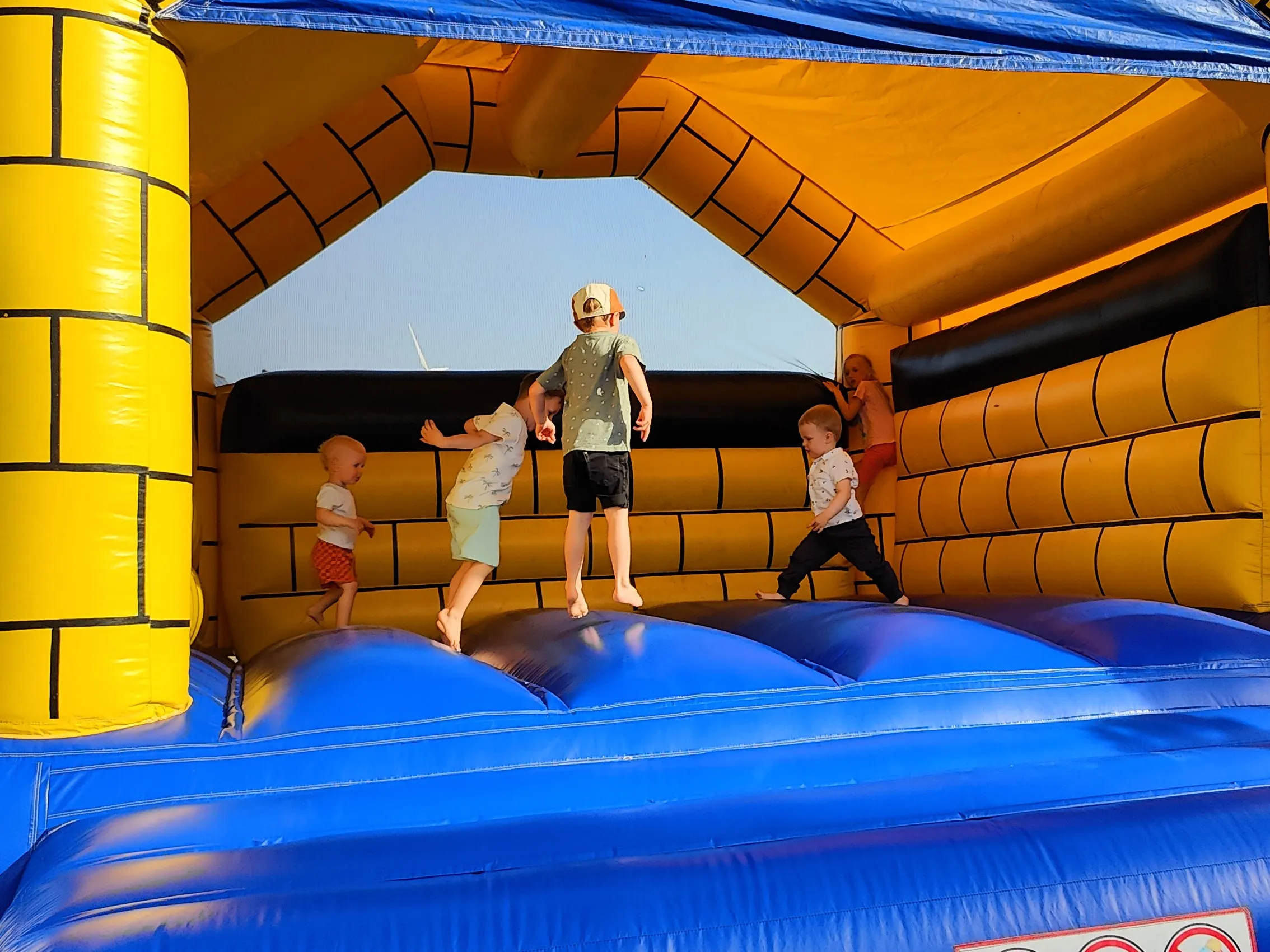 Drei Kinder spielen und springen auf einer blauen Hüpfburg mit gelben und schwarzen Burgmauern.