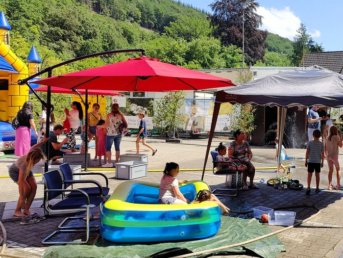 Kinder spielen und interagieren auf dem Gelände der Feuerwehr Schalksmühle während des Tages der offenen Tür. Im Hintergrund sind ein Hüpfschloss, ein Zelt und ein roter Sonnenschirm zu sehen.