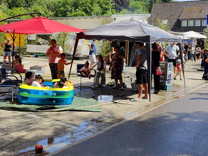 People gather at an open-air event with a small paddling pool for children and a refreshment stand, likely a fire department open day.