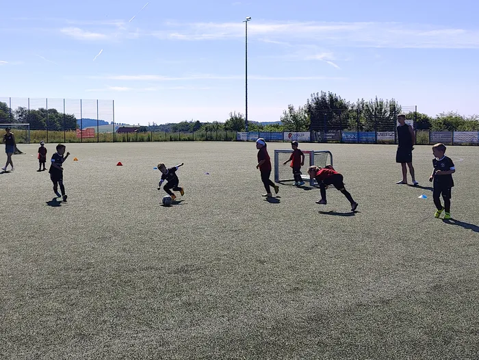 Kinder spielen Fußball auf einem Sportplatz. Im Hintergrund steht ein Mann und beobachtet das Spiel.
