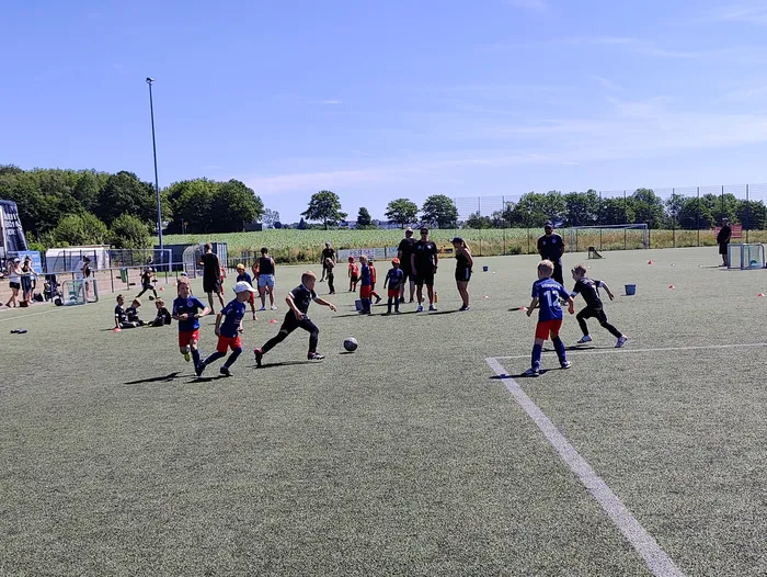 Fußballtraining mit Kindern und Jugendlichen auf einem Kunstrasenplatz. Mehrere Spieler in verschiedenen Trikots sind in Bewegung, während Trainer und Zuschauer zusehen.