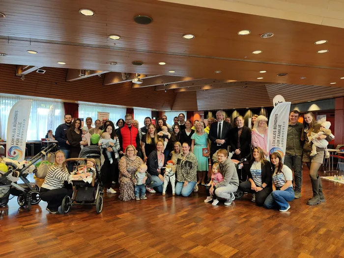 Eine große Gruppe von Menschen mit Babys und Kleinkindern posiert für ein Gruppenfoto beim Neugeborenen-Empfang im Kulturhaus Lüdenscheid.