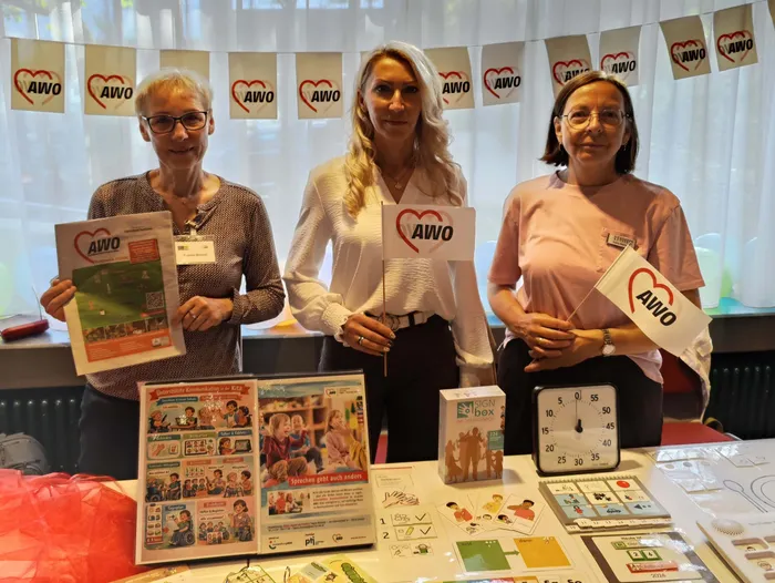 Drei Frauen der AWO stehen hinter einem Tisch mit Informationsmaterial und halten AWO-Schilder und Broschüren.