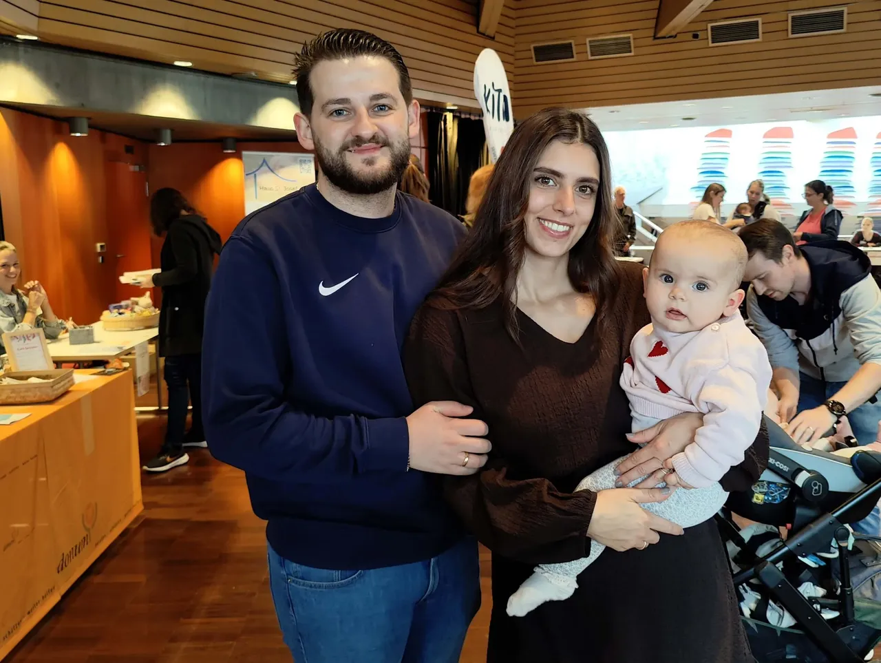 Ein lächelndes Paar mit einem Baby posiert bei einem Neugeborenen-Empfang im Kulturhaus Lüdenscheid.