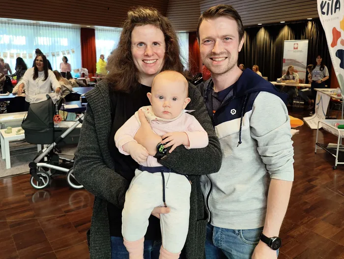Eine lächelnde Frau hält ein Baby im Arm, neben ihr steht ein lächelnder Mann bei einem Neugeborenen-Empfang im Kulturhaus Lüdenscheid.
