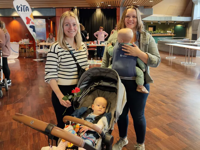 Zwei Frauen mit einem Baby in einer Trage und einem Baby in einem Kinderwagen bei einem Neugeborenen-Empfang.