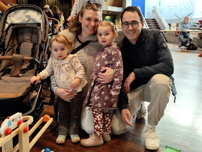 Eine lächelnde Familie mit zwei Kleinkindern posiert bei einem Neugeborenen-Empfang.