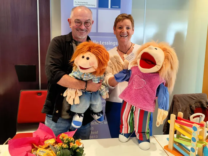 Ein Mann und eine Frau präsentieren zwei Handpuppen mit roten und blonden Haaren.