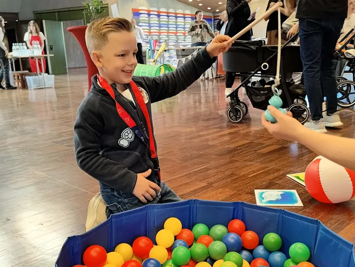 Ein lächelnder Junge spielt bei einem Neugeborenen-Empfang neben einem blauen Bällebad mit bunten Bällen.