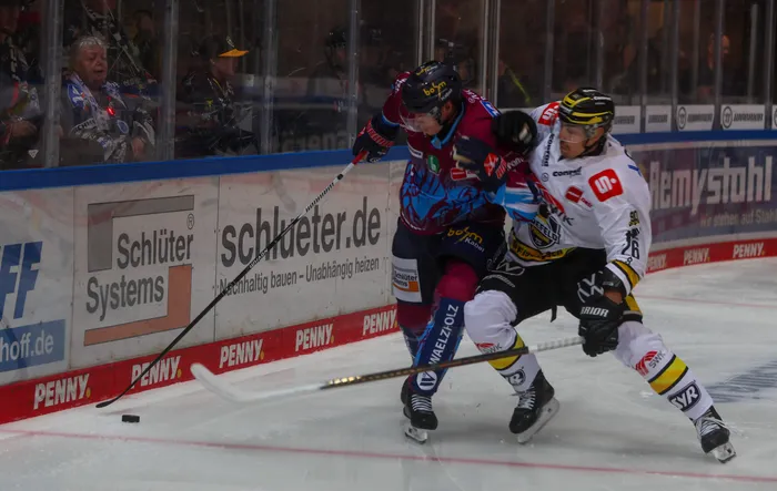 Zwei Eishockeyspieler der Iserlohn Roosters und der Krefeld Pinguine im Zweikampf auf dem Eis.