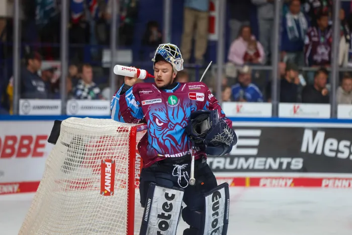Ein Eishockey-Torwart der Iserlohn Roosters trinkt neben dem Tor auf dem Eis aus einer Wasserflasche.