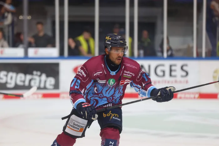 Ein Eishockeyspieler der Iserlohn Roosters in weinroter und blauer Uniform auf dem Eis.