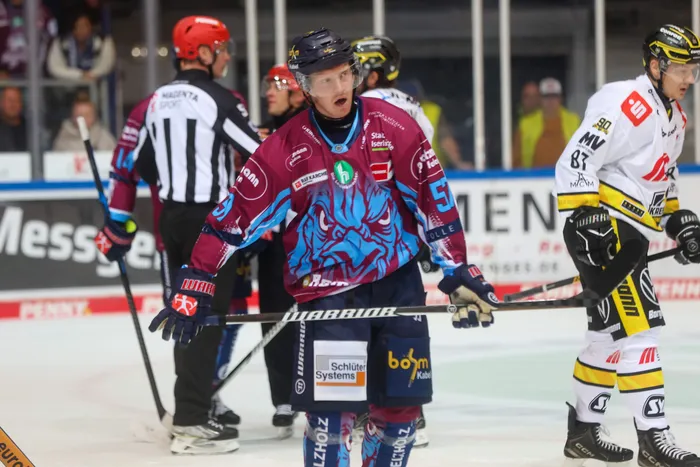 Ein Eishockeyspieler der Iserlohn Roosters in einem blau-weinroten Trikot blickt auf dem Eis nach oben.