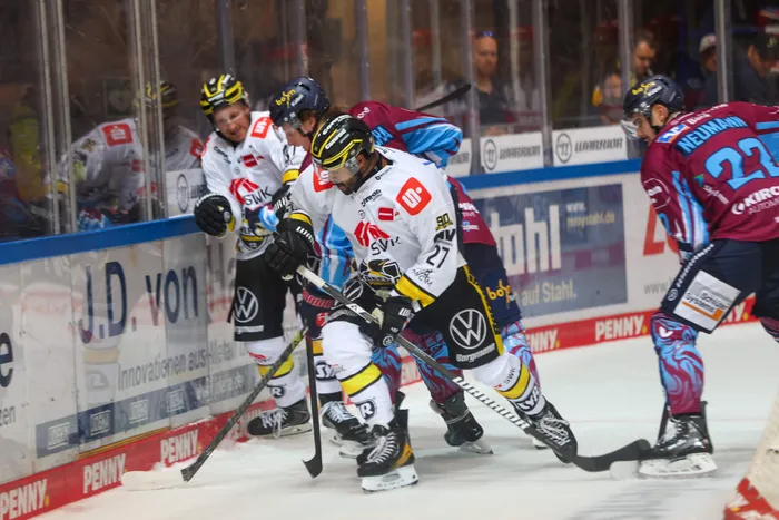 Eishockeyspieler der Iserlohn Roosters und der Krefeld Pinguine im Zweikampf um den Puck an der Bande.