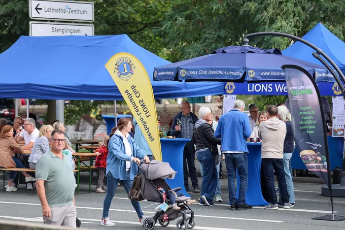Menschen auf dem Brückenfest unter blauen Zelten und Sonnenschirmen, im Vordergrund schiebt eine Frau einen Kinderwagen.