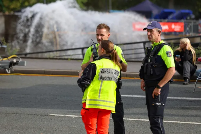 Ein Polizist und eine Einsatzleiterin im Gespräch auf einer Straße vor einem Wasserstrahl.