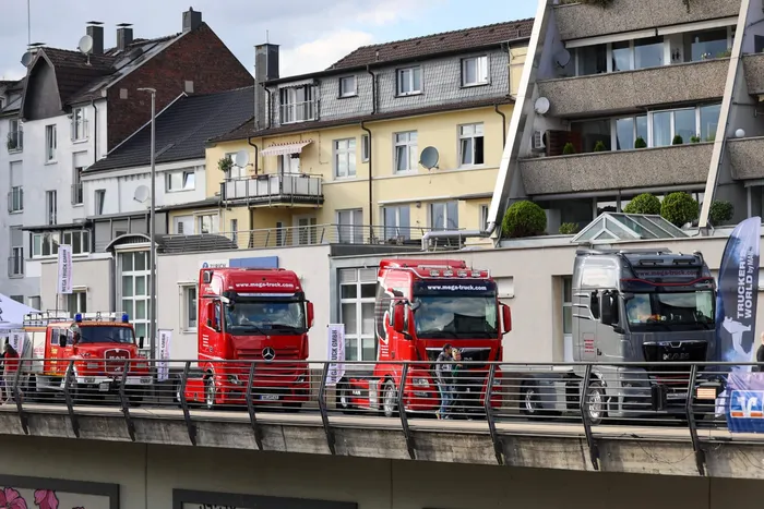 Ein Feuerwehrauto und drei große Lastwagen stehen auf einer Brücke vor Wohnhäusern.