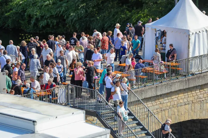 Menschen auf einer Steinbrücke mit Tischen und einem weißen Festzelt während des Brückenfests.