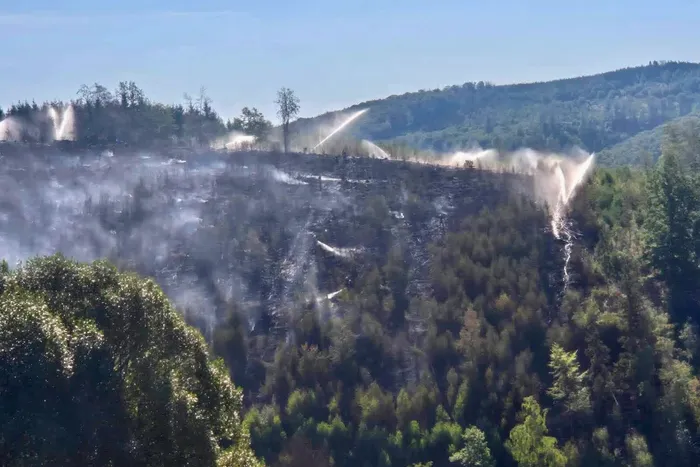 Wasserstrahlen bekämpfen einen Waldbrand in einem verrauchten, verkohlten Waldgebiet in Marsberg-Helminghausen.