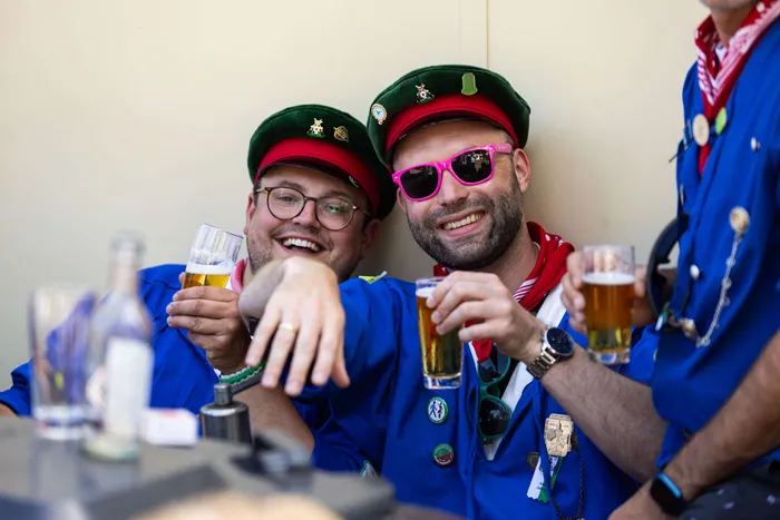Zwei Männer in traditioneller Schützenkleidung mit Hüteln stoßen mit Biergläsern an und lächeln in die Kamera.