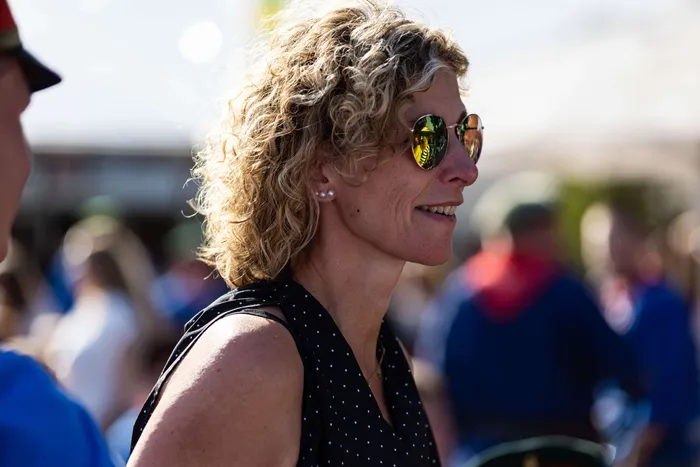 Eine Frau mit lockigem blonden Haar und Sonnenbrille blickt zur Seite, im Hintergrund Menschen auf dem Schützenfest.