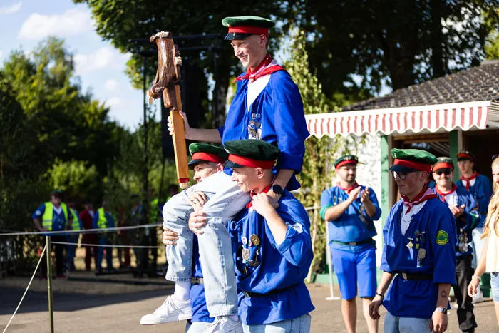 Mehrere Jungschützen in blauen Uniformen und grünen Mützen tragen einen Schützenprinzen auf ihren Schultern durch das Gelände.