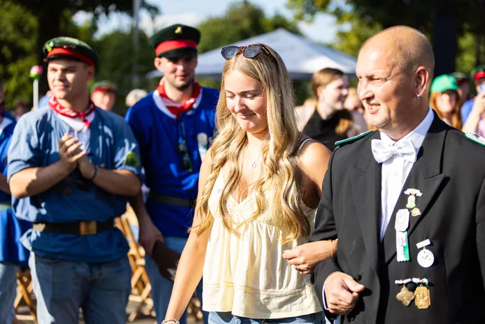 Eine junge Frau und ein Mann in festlicher Tracht gehen lächelnd durch die Menge beim Schützenfest in Meinerzhagen. Im Hintergrund sind weitere Menschen und Schützen zu sehen.