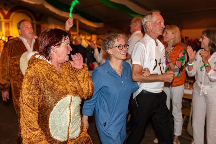Menschen tanzen bei einem Schützenfest, darunter eine Person in einem braunen Plüschkostüm.