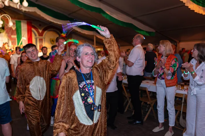Eine Frau in einem braunen Plüschkostüm hält einen leuchtenden Stab hoch, während Menschen bei einem Schützenfest feiern.