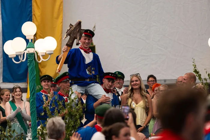 Luca Benninghaus wird nach dem Schützenfest-Schießen von seinen Kameraden auf den Schultern getragen und hält dabei ein großes hölzernes Schützenzeichen.