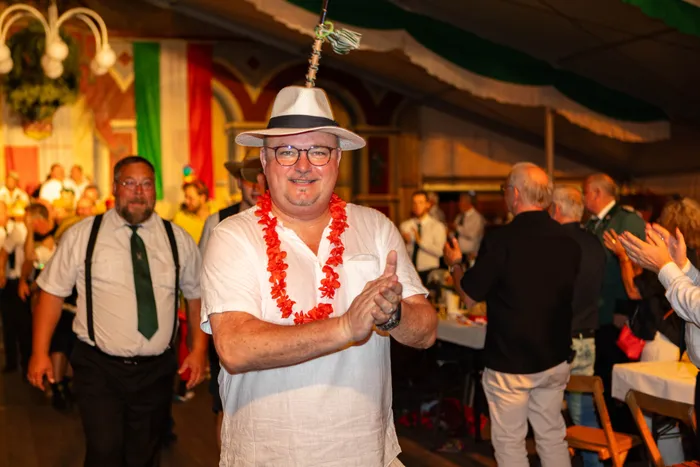 Ein lächelnder Mann mit weißem Hut und roter Blumenkette klatscht bei einem Schützenfest.