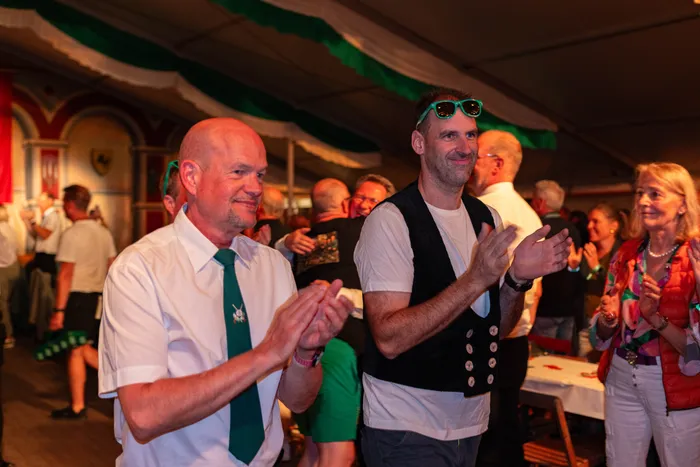 Menschen klatschen bei einem Schützenfest; im Vordergrund stehen ein Mann mit weißem Hemd und grüner Krawatte sowie ein Mann mit schwarzer Weste.
