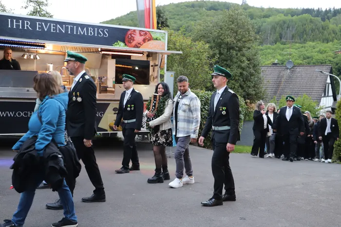 Kimberly Walter, die neue Schützenkönigin, wird von uniformierten Männern und Frauen begleitet, während sie an einem Imbisswagen vorbeigeht.