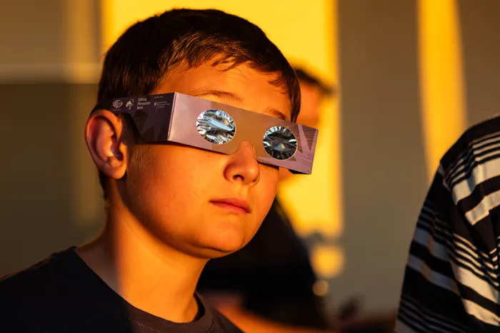Ein Junge trägt eine Pappenbrille mit reflektierenden Folienkreisen vor den Augen.