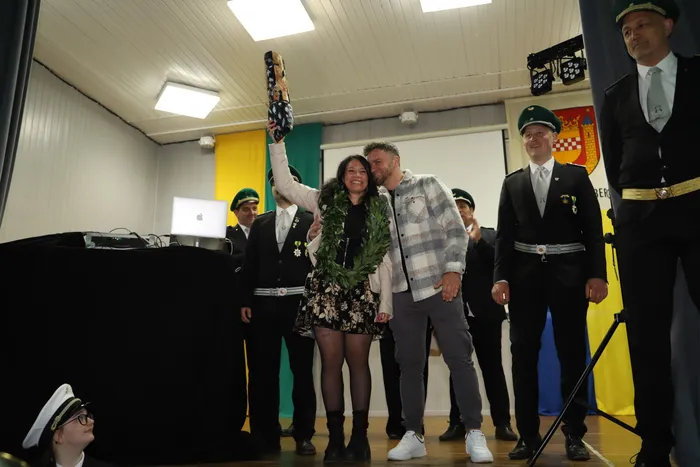 Kimberly Walter hält als neue Schützenkönigin in Landemert den Schützenvogel hoch, umgeben von Ehrengästen in Uniformen.
