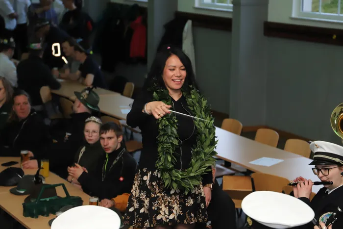 Kimberly Walter lächelt und hält einen Taktstock, umgeben von Menschen in Uniformen und Zivilkleidung während der Proklamation zur neuen Schützenkönigin in Landemert.