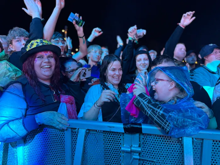 Begeisterte Menschen jubeln und lachen hinter einer Metallabsperrung bei einem nächtlichen Musikfestival.
