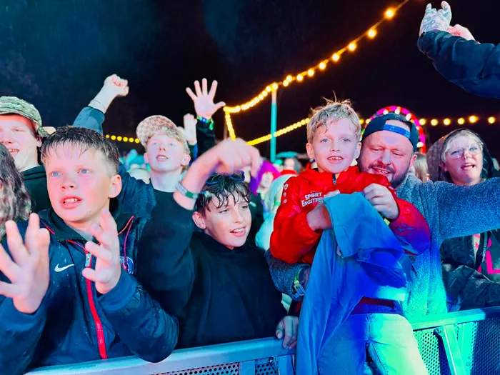 Jubelnde Menschenmenge bei einem Event, im Vordergrund ein Junge in einer roten Jacke unter Lichterketten.