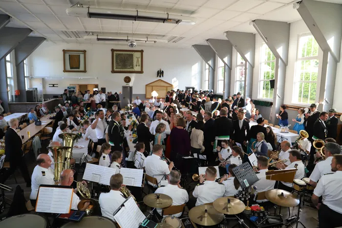 Großer Festsaal gefüllt mit Menschen bei einem Schützenfest, im Vordergrund spielt eine Blaskapelle mit verschiedenen Instrumenten.