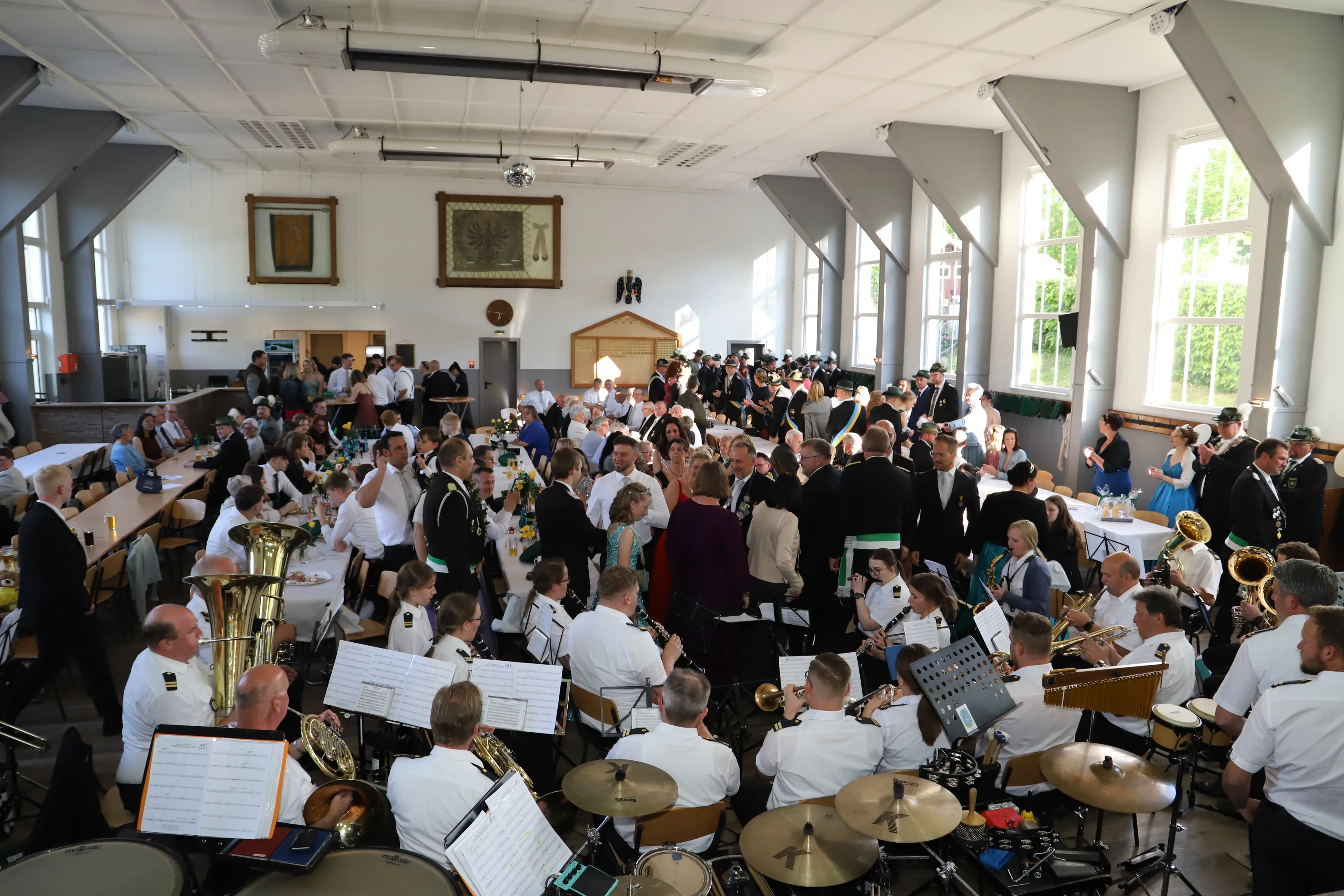 Großer Festsaal gefüllt mit Menschen bei einem Schützenfest, im Vordergrund spielt eine Blaskapelle mit verschiedenen Instrumenten.
