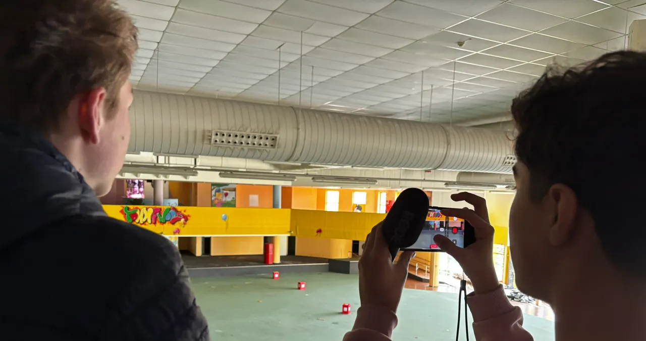 Zwei Jugendliche filmen in der leeren Halle des ehemaligen Wellenbads im Forum. Im Hintergrund eine gelb-grüne Wandgestaltung.