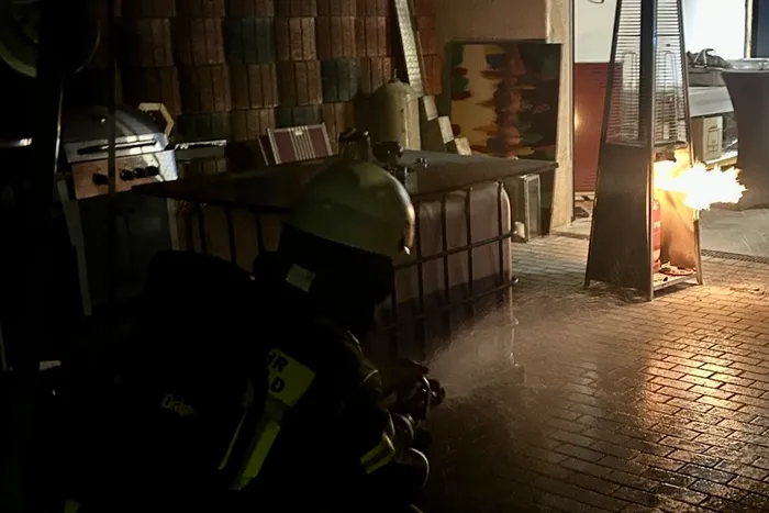 Ein Feuerwehrmann löscht nachts ein Feuer in einem Flammenheizer mit einem Wasserstrahl.