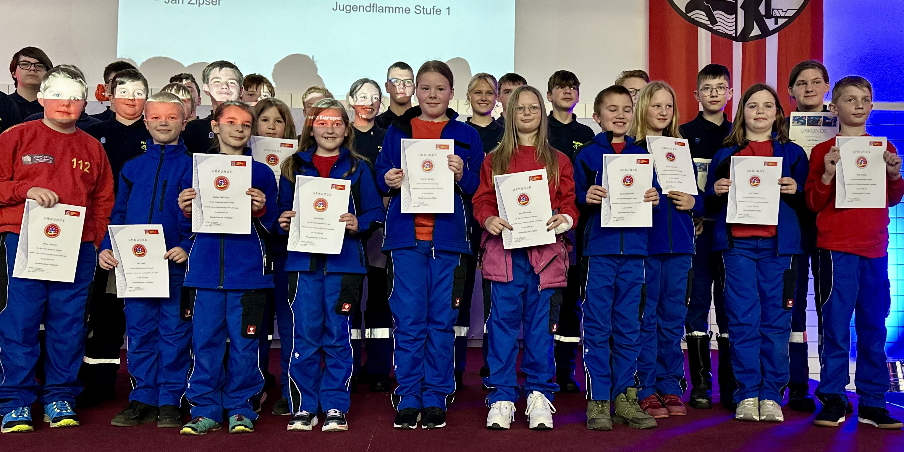 Gruppe von Kindern und Jugendlichen in Trainingsanzügen mit Urkunden der Jugendflamme Stufe 1 vor einer Bühne.