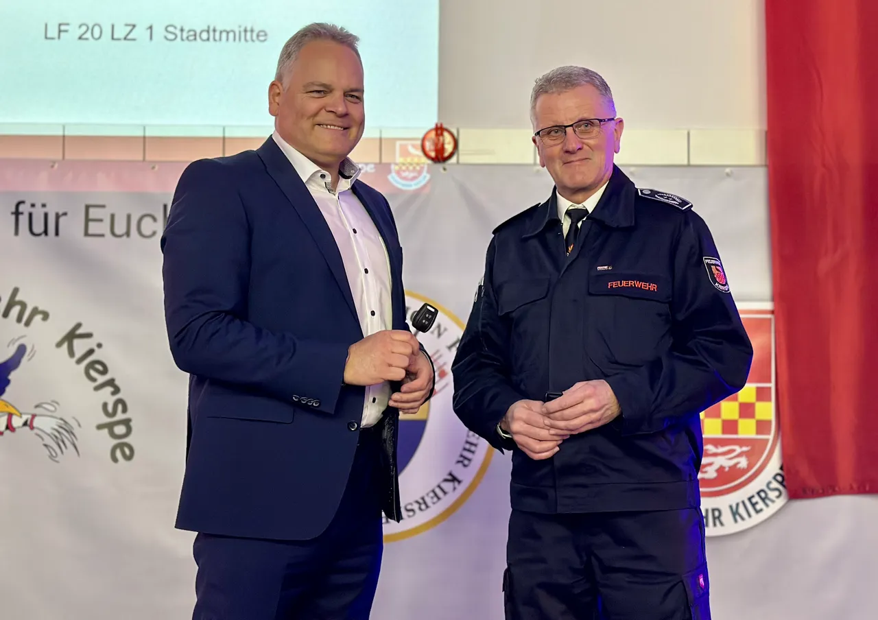 Bürgermeister Olaf Stelse und Feuerwehrleiter Mike Budde stehen auf der Bühne und sprechen in ein Mikrofon. Im Hintergrund ein Banner mit dem Aufdruck „Feuerwehr“ und dem Stadtwappen.