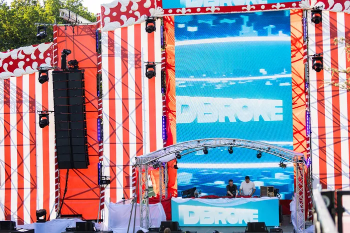 Festivalbühne mit rot-weiß gestreiftem Hintergrund, einer großen blauen Leinwand mit dem Schriftzug „DBROKE“ und zwei DJs an einem Pult.