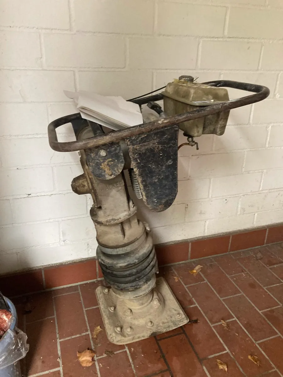 Schmutzige, gebrauchte Rüttelplatte steht auf einem roten Fliesenboden vor einer weißen Ziegelwand.