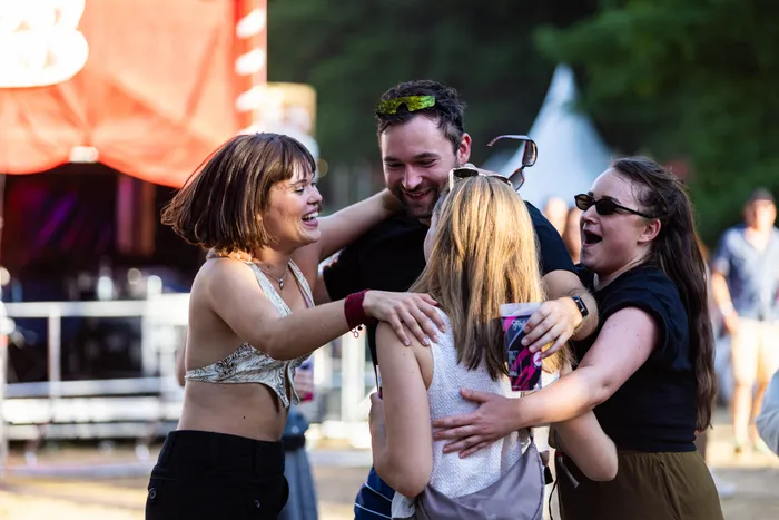 Lachende junge Menschen umarmen sich bei einem Festival im Freien.