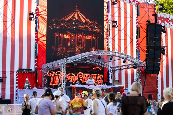 Bühne des Ferik Festivals mit einem großen Karussell-Hintergrundbild, einem DJ unter einer Überdachung und einer Menschenmenge im Vordergrund.