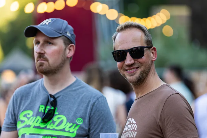 Zwei Männer beim Ferik Festival, einer trägt eine graue Kappe, der andere eine Sonnenbrille und lächelt.