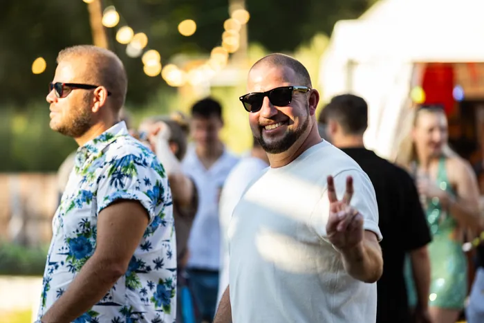 Ein lächelnder Mann mit Sonnenbrille und weißem T-Shirt zeigt das Peace-Zeichen beim Ferik Festival.
